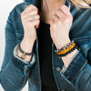 woman wearing stack of crystal bead bracelets; hematite with coin; black giraffe agate with cz ring, polished honey citrine, lava rock