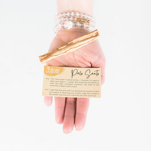 hand holding palo santo piece and informational card that explains how and why to use this smudge stick